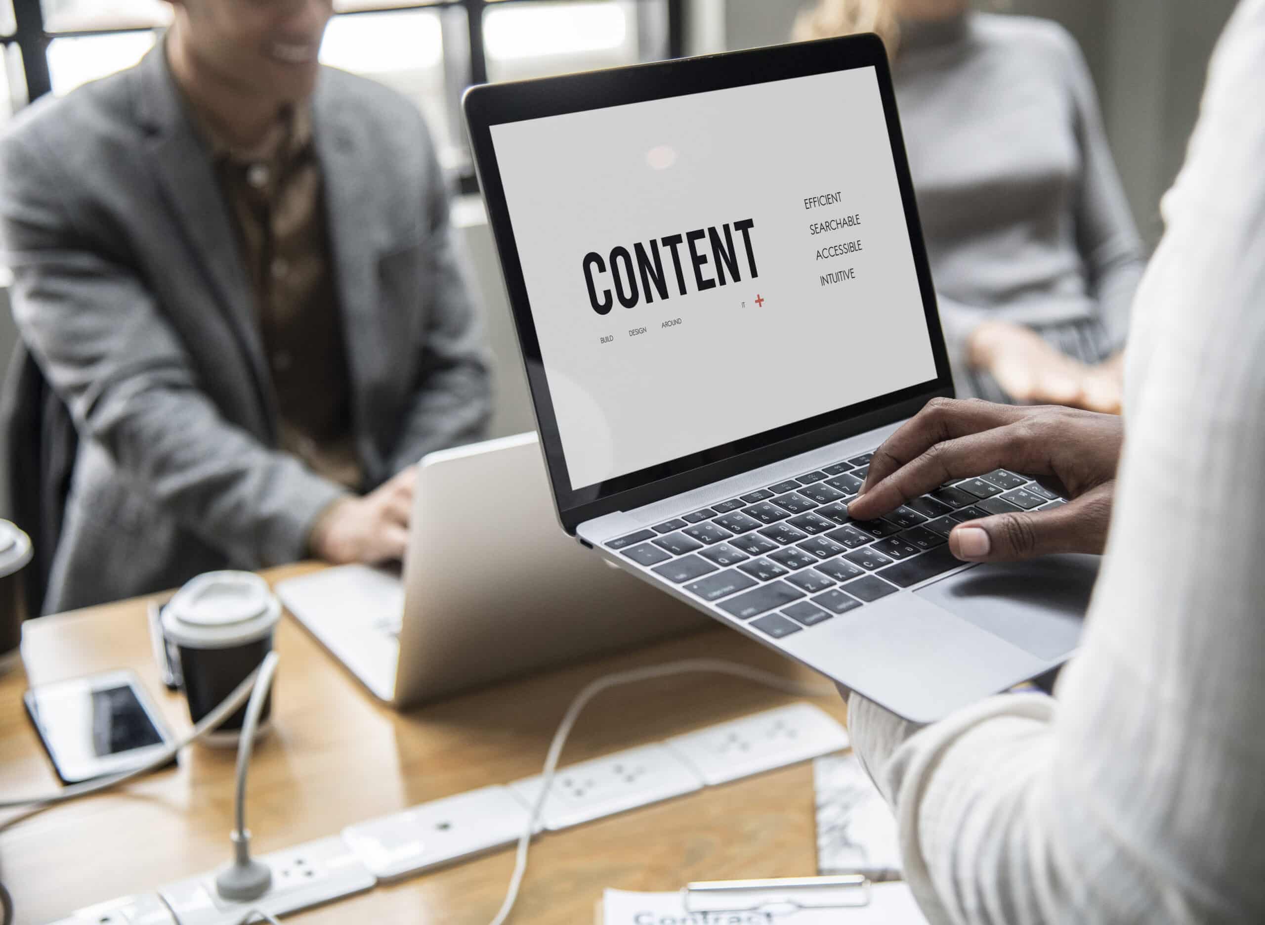 Someone typing on a laptop showing the word CONTENT during a team meeting, illustrating SEO content marketing planning ideas.