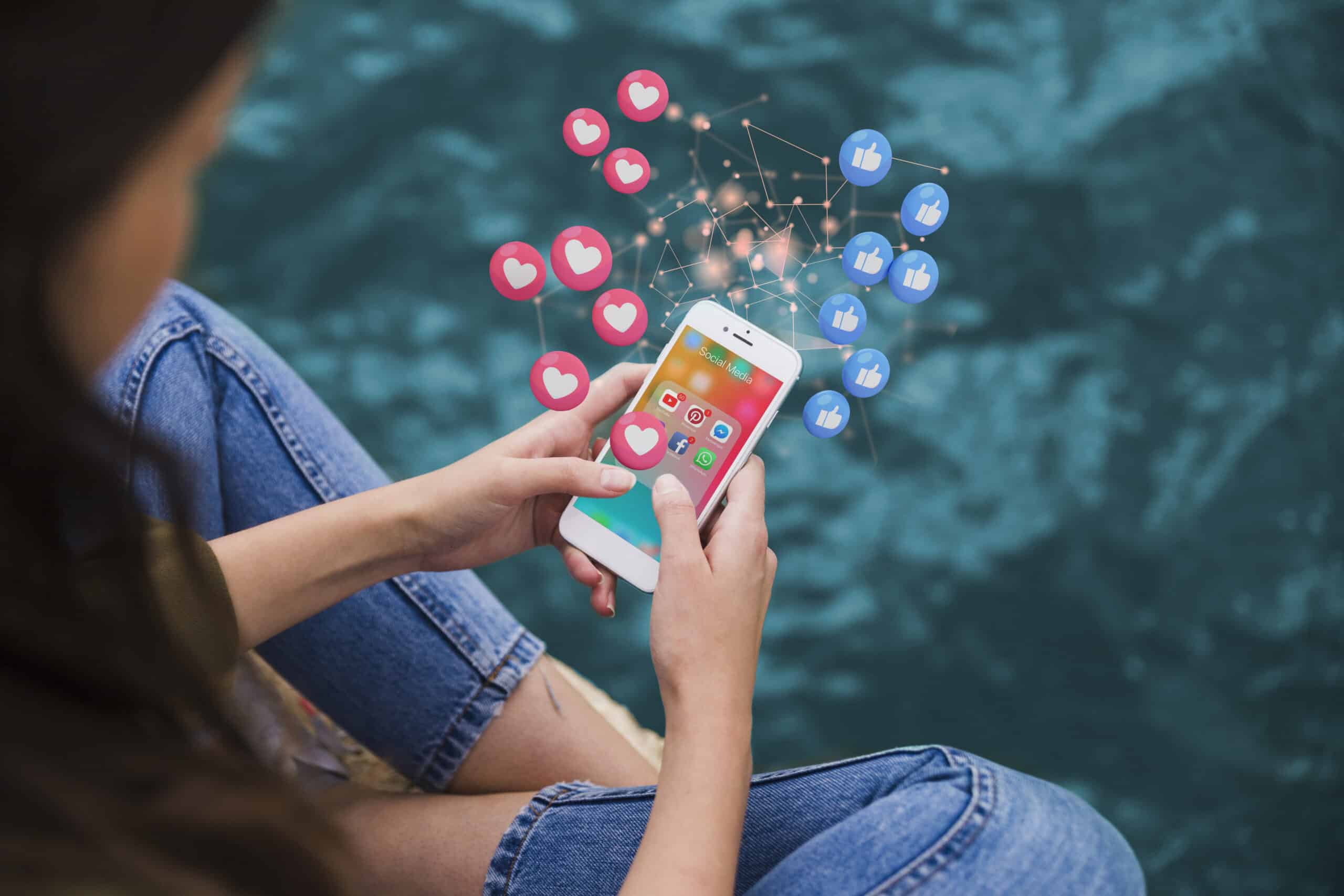 Woman holding a phone with a social media folder as floating hearts and thumbs-up icons rise, showing viral marketing reach.