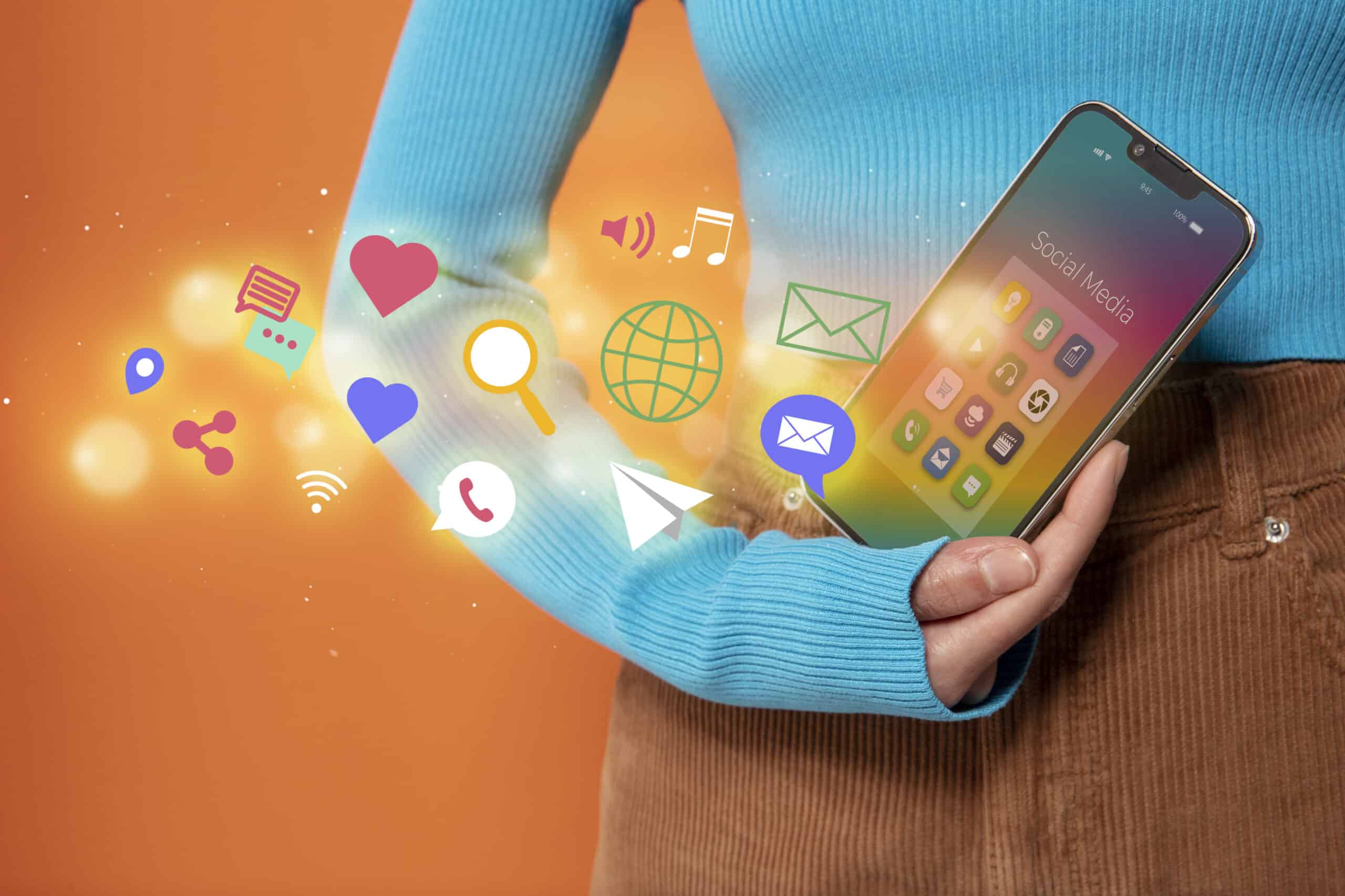 Person holding a smartphone with colorful app icons floating out, illustrating social media marketing strategies.