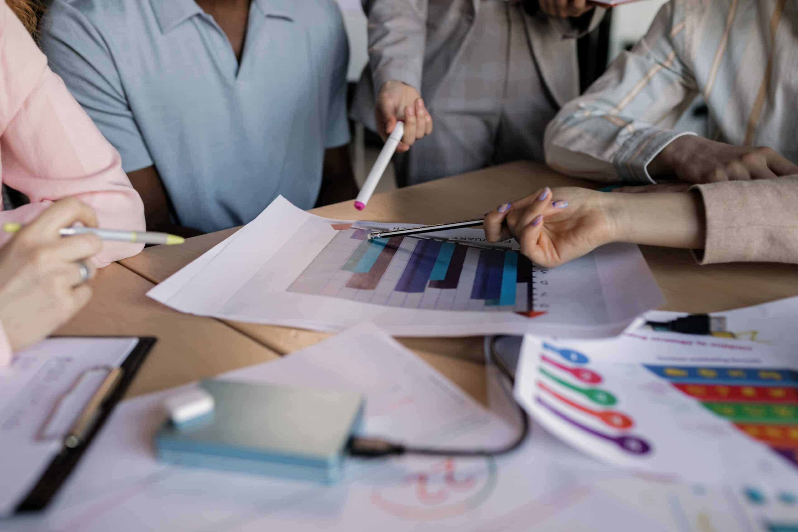 Team members pointing at printed sales bar charts and colorful graphs on a table while planning how to promote the business.